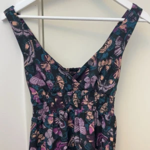 Blommig klänning  - Säljer en färgglad klänning med blommigt mönster i lila, rosa och gröna toner. Klänningen är andvänd några gånger för något år sedan. Men är nu för liten. Meddela mig om det är några minsta funderingar💕