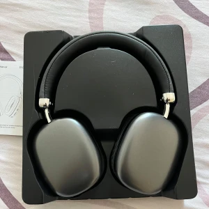 Svarta hörlurar i kartong - Snygga svarta hörlurar med vadderade öronkuddar och justerbart huvudband. Perfekt för musikälskare som vill ha stil och komfort. Levereras i originalförpackning.