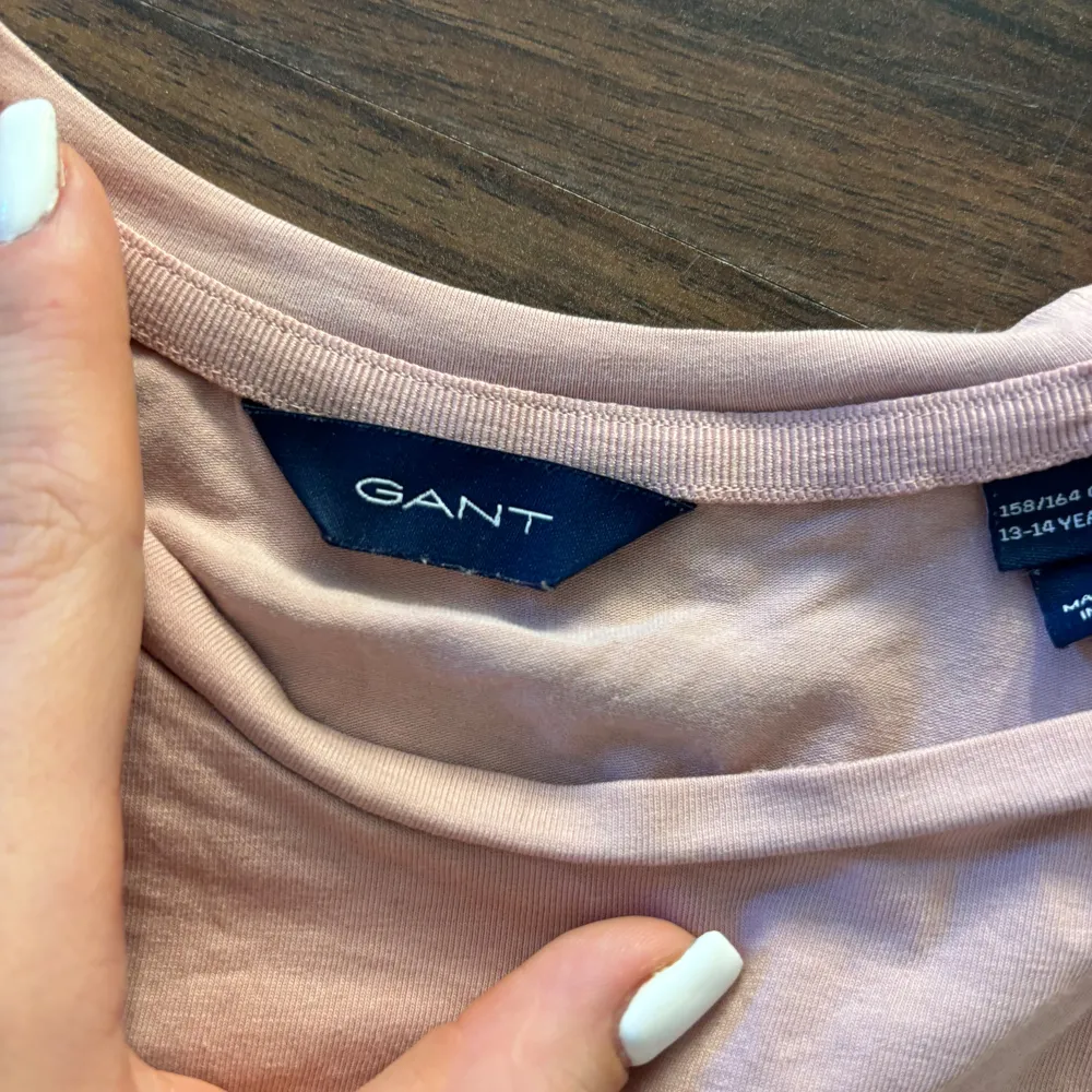 Säljer en rosa t-shirt från GANT med tryck i guld på framsidan. T-shirten har en rund hals och korta ärmar. Perfekt för en avslappnad stil.. T-paidat.