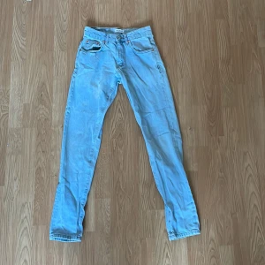 Ljusblå jeans från Woodbird - Snygga ljusblå jeans från Woodbird med klassisk femficksdesign och knappgylf. Perfekta för en avslappnad stil. Märkesdetalj i läder baktill vid midjan. Knappt använda - ser helt nya ut