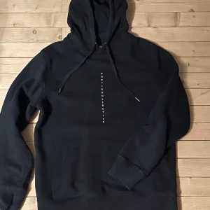 Svart hoodie från Poetic Collective - Snygg svart hoodie från Poetic Collective, säljer då den ej används. Använd få gånger riktigt bra skick. unik konstnärlig design på baksidan. Tröjan har en klassisk känguruficka och justerbar huva med snören. Perfekt för en stilren och avslappnad look. 
