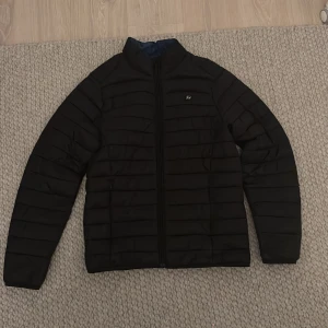 Svart pufferjacka från Blend - Säljer en svart pufferjacka från Blend i storlek S. Jackan har en dragkedja framtill och är långärmad. Insidan är fodrad i en mörkblå nyans för extra värme och stil.