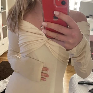 Beige offshoulder klänning - Säljer en elegant beige offshoulder tröja med långa ärmar. Tröjan har en unik draperad detalj framtill som ger en stilren look. Perfekt för en chic och sofistikerad stil. Passar utmärkt för speciella tillfällen. Storlek M men passar S och XS