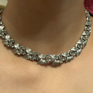 Silverfärgat halsband med blommotiv - Elegant silverfärgat halsband med detaljerade blommotiv och glittrande stenar. Perfekt för att ge en sofistikerad touch till din outfit. Halsbandet har en kedja med justerbar längd för bästa passform.