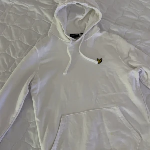 Vit hoodie från Lyle & Scott - Säljer en stilren vit hoodie från Lyle & Scott med deras ikoniska logga på bröstet. Tröjan har en klassisk känguruficka och justerbar huva med snören. Perfekt för en avslappnad look. Storlek S. Ny pris kostar: 849. Säljer för 300.
