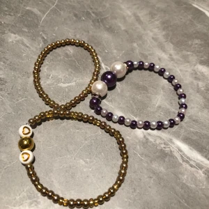Set med tre pärlarmband - Snyggt set med tre elastiska pärlarmband. Ett armband i guldton med små pärlor, ett med lila och vita pärlor samt ett med guldpärlor och vita detaljer med hjärtan. Perfekt för att mixa och matcha! Passar till dom med lite mindre handled. 150kr för alla 50 för ett