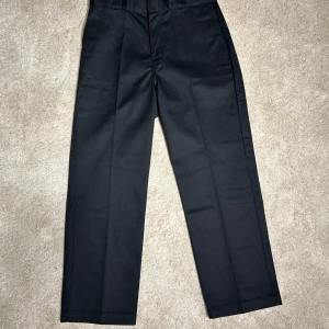 Dickies - Snygga svarta kostymbyxor från Dickies med klassisk design. Byxorna har en rak passform och är tillverkade i ett slitstarkt material. Perfekta för en stilren look.