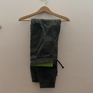 Gröna cargopants med broderad detalj - Snygga gröna cargopants med broderad detalj på fickan. Byxorna har en avslappnad passform med elastiska muddar vid bensluten och praktiska fickor. Perfekta för en casual look. Är i storlek 170 14 år men skulle kunna passa en xs.