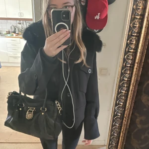 Svart Meotine kappa  - Snygg slutsåld svart kappa från Meotine, med pälsdetaljer på kragen. Nypris 3500kr. Jackan har långa ärmar och knappar framtill. Perfekt för kyligare dagar och ger en elegant look. Storlek xs/s. Kan mötas upp i Stockholm, Tyresö eller Haninge. 