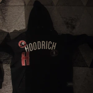 Svart hoodie från Hoodrich - Snygg svart hoodie från Hoodrich med stora bokstäver på framsidan. Den har en klassisk huva och långa ärmar. Perfekt för en avslappnad stil. Testa att buda!!