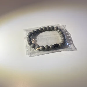 Grått Pärlarmband AllCap - Snyggt grått armband med runda stenar och en svart detalj. Perfekt accessoar för en stilren look. Elastiskt band för enkel passform. Skick 10/10