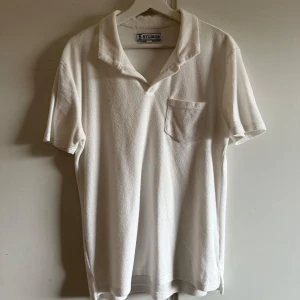 Vit kortärmad t-shirt från s&t Studios - Säljer en stilren vit t-shirt från Studios med korta ärmar och en klassisk krage. T-shirten har en bröstficka och är tillverkad i ett mjukt material som ger en bekväm passform. Perfekt för en avslappnad look.