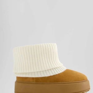 Bruna boots med vit ribbad kant - Säljer ett par bruna boots med en mysig vit ribbad kant. Skorna har en rund tå och en robust sula, perfekt för kyligare dagar. Insidan verkar vara fodrad för extra värme.