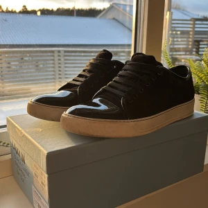 Svarta sneakers från Lanvin - Snygga svarta sneakers från Lanvin med glansig finish och klassisk snörning. Skorna har en vit sula som ger en stilren kontrast. Perfekta för en trendig look.