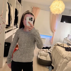 Grå stickad tröja från H&M - Mysig grå stickad tröja från H&M med kabelstickat mönster. Perfekt för kyliga dagar med sin klassiska design och bekväma passform. Tröjan har långa ärmar och ribbade kanter vid ärmslut och nederkant.
