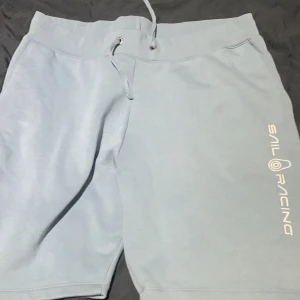 Ljusblå shorts från Sail Racing - Snygga ljusblå shorts från Sail Racing med dragsko i midjan för justerbar passform. Perfekta för en avslappnad stil. Logotypen är tryckt i vitt på benet.