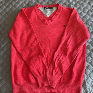 Röd v-ringad tröja Polo Ralph Lauren - Röd v-ringad tröja från Polo Ralph Lauren med klassisk broderad logga på bröstet. Tröjan har långa ärmar, ribbade muddar och är i ett mjukt, tunt material som passar perfekt till lager-på-lager. Enkel och stilren design som funkar till allt.