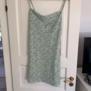 Grön blommig klänning  - Aldrig använd. Det går att spänna banden. Finns ett band i midjan. Den är mer ljusgrön än av den ser ut på bilderna. 