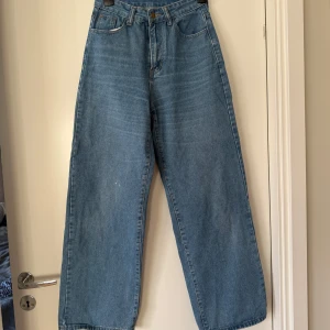 Blåa wide jeans med hög midja - •Säljer ett par ljusblå jeans med hög midja och breda ben.  •Klassisk femficksmodell med raka sömmar och dragkedja framtill.  •Perfekta för en avslappnad och trendig look. •Mycket bra skick, förutom att det finns en liten vit fläck(se bild), därav priset. •Storlek S. •Djurfritt och rökfritt hem.