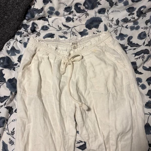 Vita linnebyxor från Roxy med snörning - Säljer ett par vita linnebyxor från Roxy med avslappnad passform. Byxorna har elastisk midja med snörning och stora fickor framtill. Perfekta för chill dagar eller strandhäng. Lätta och luftiga i materialet linne. De är i storlek M men sitter bra på mig som brukar använda XS/S W26/27