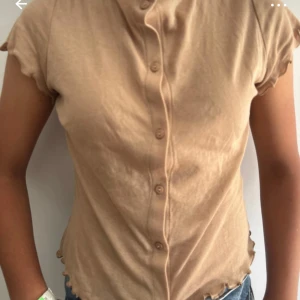 Beige blus med vågig kant Primark - Säljer en beige blus från Primark i storlek S. Toppen har korta ärmar, knappar framtill och vågiga kanter vid ärmslut och nederkant. Perfekt för dig som gillar en enkel men ändå söt stil.
