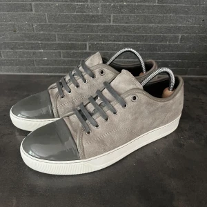 Grå mockasneakers med lackad tå lanvin  - Svin snygga lanvin i ljusgrå mocka med grå snörning och vit sula. Storlek in 7 sitter som 42-43. Otroligt bra skick som nya 9/10 använda en handfull av gånger. Sulkräm har använts för att fräscha upp skorna lite extra
