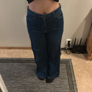 Mörkblå wide jeans från Lee - Säljer ett par mörkblå jeans från Lee med hög midja och breda ben. Klassisk femficksmodell med snygga kontrastsömmar och Lee-logga på bakfickan. Jeansen är i kraftig denim och har dragkedja framtill.