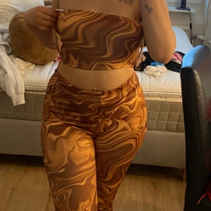 Multifärgat sett - Säljer ett matchande sett med swirlmönster i olika nyanser av brunt och beige. Toppen är axelbandslös och sitter tight mot kroppen, perfekt för dig som vill sticka ut med ett coolt mönster. 