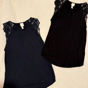 Två ärmlösa toppar med spetsdetaljer - Säljer två snygga ärmlösa toppar från H&M, en i marinblått och en i svart. Båda har vackra spetsdetaljer på axlarna och en rund halsringning. Perfekta att styla med jeans eller kjol för en trendig look. Paketpris: 125 kr. Aldrig använda.