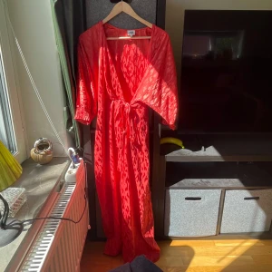 Röd omlottklänning Twist & Tango - Snygg röd långklänning från Twist & Tango med leopardmönster. Omlottmodell med knyt i midjan och v-ringning. Klänningen har trekvartsärmar med resår vid ärmslut och ett lätt glansigt tyg. Som ny!!!