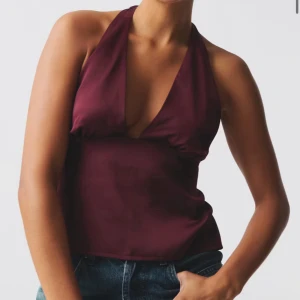 Vinröd halterneck topp med knyt - Säljer en vinröd halterneck topp med djup v-ringning och öppen rygg. Toppen knyts både i nacken och i ryggen för en snygg passform. Perfekt att styla med jeans eller kjol. Säljer toppen eftersom den inte var min stil. Toppen har också prislappen kvar och har aldrig använts, bara provats. Storleken passar för xs/s/m eftersom det finns knytband för att justera passformen