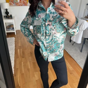 Mönstrad skjorta från Voyelles M - Snygg skjorta från Voyelles i storlek M med blommigt mönster i turkos, rosa. Skjortan har två bröstfickor, klassisk krage och knäppning framtill. Materialet känns mjukt och svalt. Finns inget att anmärka på, mycket fint skick!