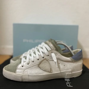 Philippe Model sneakers  - Snygga Philippe Model PRSX Low Man sneakers i vitt skinn med gröna och blå detaljer. Klassisk låg modell med vit sula, rund tå och vita snören. Sköldlogga på sidan och vintagekänsla i designen. Perfekta för dig som gillar stilrena och trendiga sneakers. Bra skick! Allt org medföljer! Storlek 41