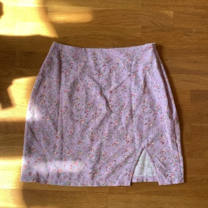 Ljuslila blommig kortkjol med slits - Superfin ljuslila miniskirt med små blommor. Kjolen har en liten slits framtill som ger en extra touch. Perfekt för dig som gillar söta och romantiska vibes. Passar till sneakers eller sandaler för en chill look. Storlek: XS men sitter som en M. Den är helt oanvänd 💞