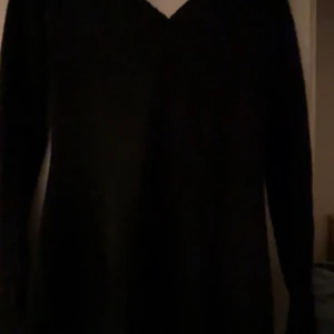 Svart långärmad klänning med v-ringning och luva - En svart klänning med lång ärm och v-ringad hals. Modellen är enkel och stilren, perfekt för dig som gillar minimalistisk look. Klänningen har en rak passform och är i ett mjukt material som känns skönt mot huden. Den har även en luva.