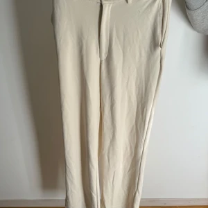Beige kostymbyxor i ”mjukis” material - Stilrena beige kostymbyxor med raka ben och hög midja. Byxorna har bälteshällor, sidofickor och stängs med knapp och dragkedja. Perfekta vardags byxor då de är i ”mjukis” material. Perfekt om man vill vara bekväm men endån stilren😍