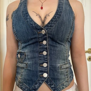 Jeansväst med knappar och bälte - En favorit som blivit för liten 💔jag skulle säga att den är en thight S, kanske XS. Snygg jeansväst i blå denim med markerad v-ringning och sex silverfärgade knappar framtill. Västen har två fickdetaljer och justerbart bälte i ryggen för perfekt passform. Figurnära modell med cool vintagekänsla, perfekt till lager-på-lager-stil.