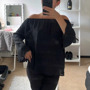 Svart offshoulder blus med vida ärmar - Säljer en svart offshoulder blus med vida, långa ärmar. Toppen har en luftig och flowy passform i ett tunt, lätt material. Den ser lite stor ut på mig men är också 1,53 så för någon som är lite längre skulle den vara perfekt