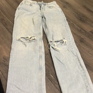 Ljusblå ripped jeans från Gina Tricot - Ljusblå jeans från Gina Tricot med raka ben och stora slitningar över knäna. Klassisk femficksmodell i denim med normal passform och hög midja. Perfekta för en avslappnad och trendig look.