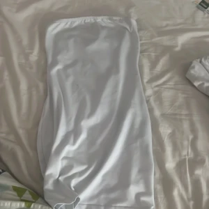 Vit axelbandslös kortklänning - Säljer en enkel och stilren vit axelbandslös kortklänning. Klänningen har en rak passform och är tillverkad i ett mjukt, slätt material som känns skönt mot huden. Perfekt för varma dagar när du vill ha en clean och fräsch look.