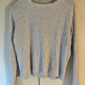 Ljusgrå långärmad tröja från H&M - En basic ljusgrå långärmad tröja från H&M i ribbad bomull. Tröjan har rund halsringning och en avslappnad passform, perfekt att styla med jeans eller mjukisbyxor. Enkel och stilren design som funkar året runt.