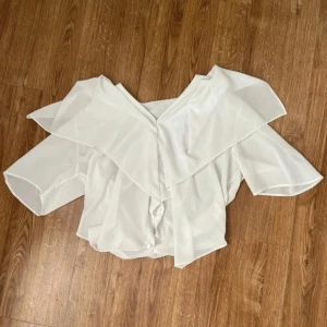 Vit blus med volangkrage - Superfin vit blus med stor volangkrage och knappar framtill. Blusen har trekvartsärm och är gjord i ett lätt, transparent tyg som ger en luftig känsla. 