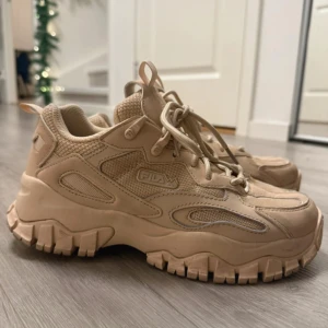 Beige chunky sneakers från Fila - Chunky sneakers från Fila i helbeige färg med grov sula och meshdetaljer. Skorna har snörning och är tillverkade i en mix av syntet och mesh för en sportig vibe. Perfekta för dig som gillar streetstyle och vill sticka ut med en robust look.