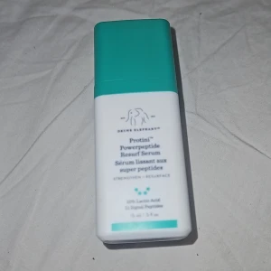 Drunk Elephant Protini Powerpeptide Serum - Protini Powerpeptide Resurf Serum från Drunk Elephant i en stilren vit och turkos plastflaska med pump. Innehåller 10% mjölksyra och 11 signalpeptider för att stärka och jämna ut huden. Perfekt för dig som vill boosta din hudvårdsrutin med peptider.