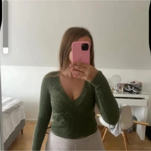 Olivgrön omlottopp från Hollister - Säljer en olivgrön ribbad omlottopp från Hollister i storlek M. Tröjan har lång ärm, v-ringning och figurnära passform. Perfekt till jeans eller kjol för en snygg och enkel look.