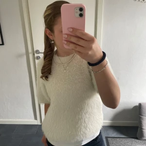 Vit fluffig stickad tröja från Wera - Supermjuk och fluffig vit stickad tröja från Wera. Tröjan har korta ärmar och rund halsringning, perfekt för dig som gillar en cozy och trendig look. Passar lika bra till jeans som till kjol. Snygg och enkel att styla året runt!