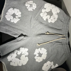 Gråa denim tears shorts - Grå shorts i mjuk bomull med elastisk midja och snörning. Shortsen har vita, molnliknande tryck över hela tyget och råa kanter vid bensluten för en avslappnad vibe. Perfekta för chill dagar eller streetwear-stil.