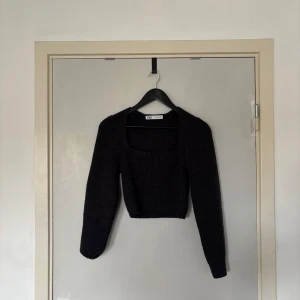 Mörkgrå croppad stickad tröja Zara - Säljer en mörkgrå croppad stickad tröja från Zara med fyrkantig urringning och långa ärmar. Tröjan har ribbad struktur och sitter snyggt med en lite tightare passform. Perfekt till höst- och vinteroutfits!