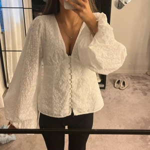 Vit blus med broderade blommor - Superfin vit blus med broderade blommor och v-ringning. Blusen har långa puffärmar, klädda knappar framtill och är gjord i ett lätt bomullstyg. Perfekt för dig som gillar romantiska detaljer och en luftig känsla. Nypris ca 800kr. Liknar adoore blusen💕