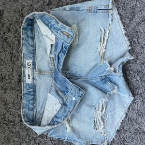 Ljusblåa jeansshorts XXS - Snygga ljusblå jeansshorts från new yorker i storlek XXS. De har flera slitningar framtill för en trendig, avslappnad look. Klassisk femficksmodell med knapp och dragkedja. Perfekta för varma dagar.